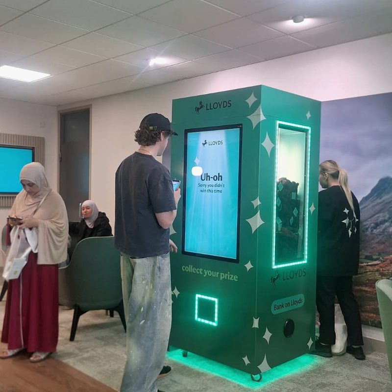 A fully wrapped digital claw machine with an on-screen game, prize window and collection hatch, guests playing
