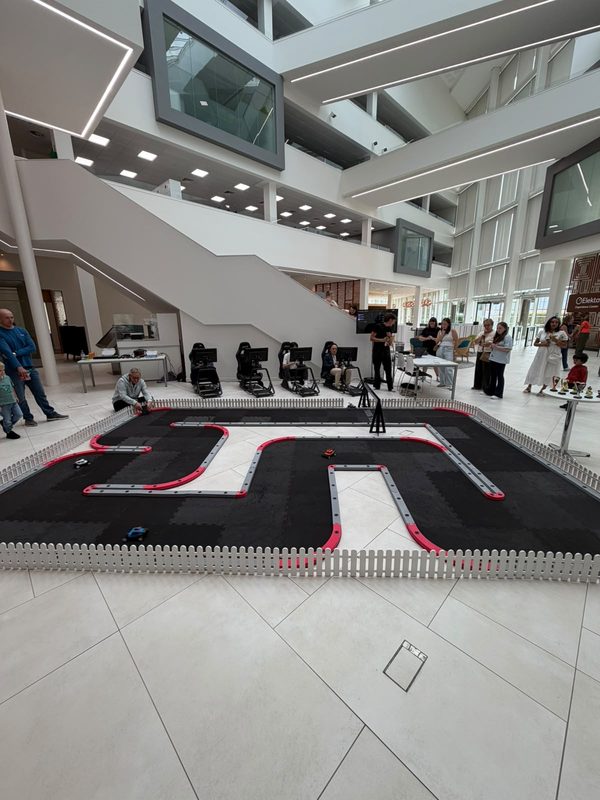 FPV RC racing track set up in an office atrium, drivers seated at screens behind it and guests watching