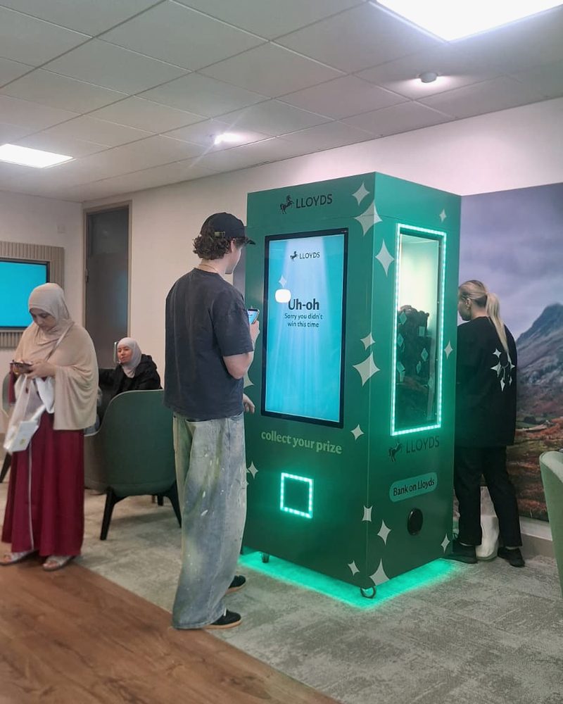 A fully wrapped digital claw machine with an on-screen game, prize window and collection hatch, guests playing